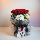 Bouquet of red roses and white flowers wrapped in black and white paper with ribbons on a blurred background