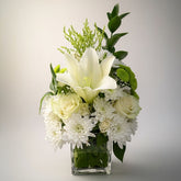 Floral arrangement with white and green flowers in a clear vase on a light background