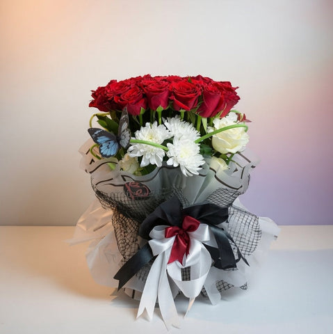 Bouquet of red roses and white flowers wrapped in black and white paper with ribbons on a blurred background