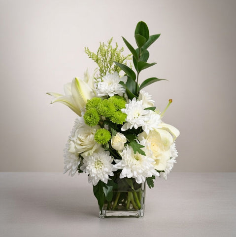 Bouquet of white and green flowers in a clear vase on a light background
