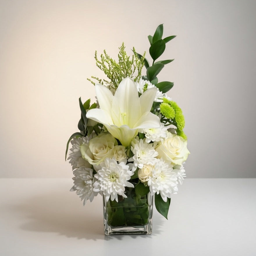 Floral arrangement with white flowers and greenery in a clear vase on a light background