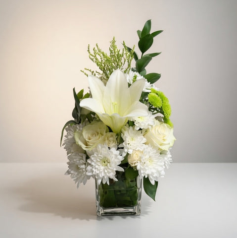 Floral arrangement with white flowers and greenery in a clear vase on a light background