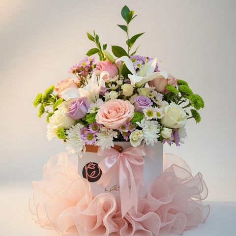 Floral arrangement in a decorative box with ruffled pink ribbon on a light background