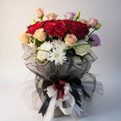 Bouquet of red, white, and pink flowers with decorative ribbons on a light background
